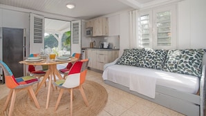 A compact living space with a dining area, kitchenette, and a sofa with a leaf-patterned cover. - F2 M'Bay : Sea & Pool access (Anse Charpentier)