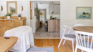 Ein gemütlicher, gut beleuchteter Raum mit einem hölzernen Bett, einem Esstisch mit Stühlen, einer Küchenzeile und einem Flur, der zu einem anderen Raum führt.