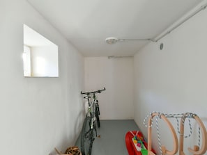 Un couloir étroit dans lequel un vélo est appuyé contre le mur, une petite voiture rouge en jouet et un porte-objets en bois avec une corde.