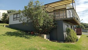 Una casa de un piso con balcón, un árbol pequeño y un patio cubierto de césped.