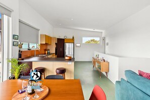A modern kitchen with a dining area, a living room with a sofa, and a view of the outdoors.