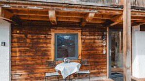 Una cabaña de madera con un pequeño patio que incluye una mesa, sillas, una ventana y una puerta.