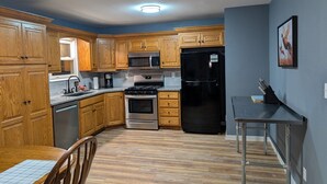 Una cocina con armarios de madera, electrodomésticos de acero inoxidable, una mesa de comedor con sillas y una encimera con cafetera.