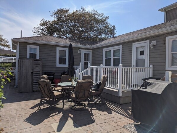 A patio with a table and chairs, a barbecue grill, and a white fence.
