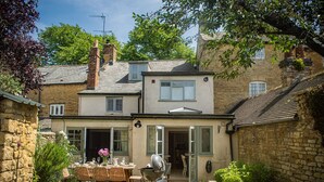 A two-story house with a patio area, a dining table, and chairs. - Beautifully presented holiday cottage - Stonecrop Cottage (Moreton-in-Marsh)