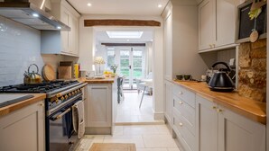 A modern kitchen with a central island, a stove, and a kettle. There is a view of a garden through the window. - Beautifully presented holiday cottage - Stonecrop Cottage (Moreton-in-Marsh)