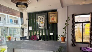 A reception area with a marble counter, framed religious artwork, potted plants, and a view of the outside. - Shree Radhe Mohan Hotel and Resort (Danta Ramgarh)