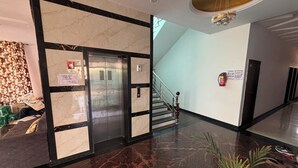 A lobby with a marble wall, an elevator, a staircase, and a fire extinguisher. - Shree Radhe Mohan Hotel and Resort (Danta Ramgarh)