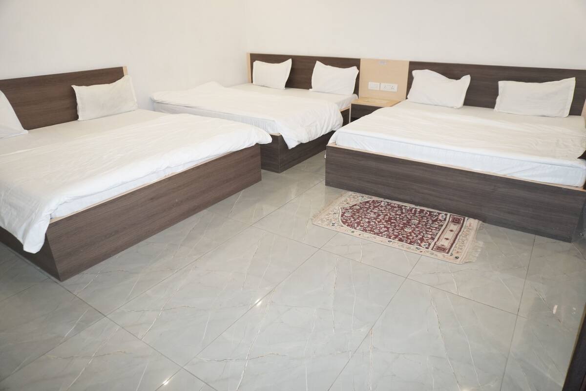 Habitación de hotel con cuatro camas dispuestas en una esquina, piso de baldosas y una alfombra decorativa.