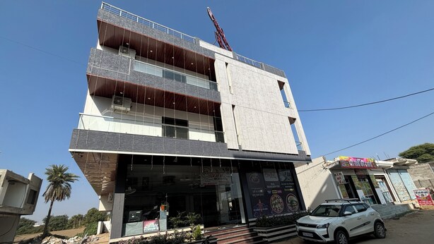 A multi-story building with a restaurant on the ground floor, featuring a large glass entrance and outdoor seating area. - Shree Radhe Mohan Hotel and Resort (Danta Ramgarh)