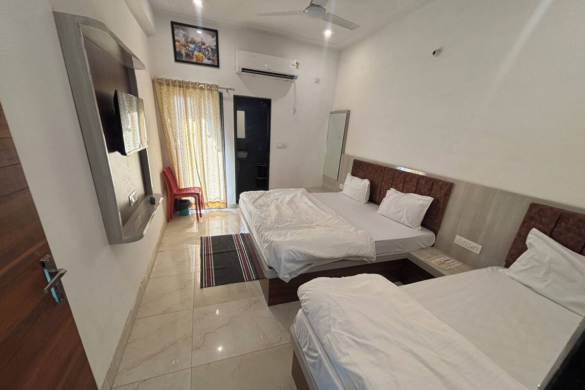 Habitación de hotel con dos camas, un televisor, un ventilador de techo y un baño visible a través de una puerta.