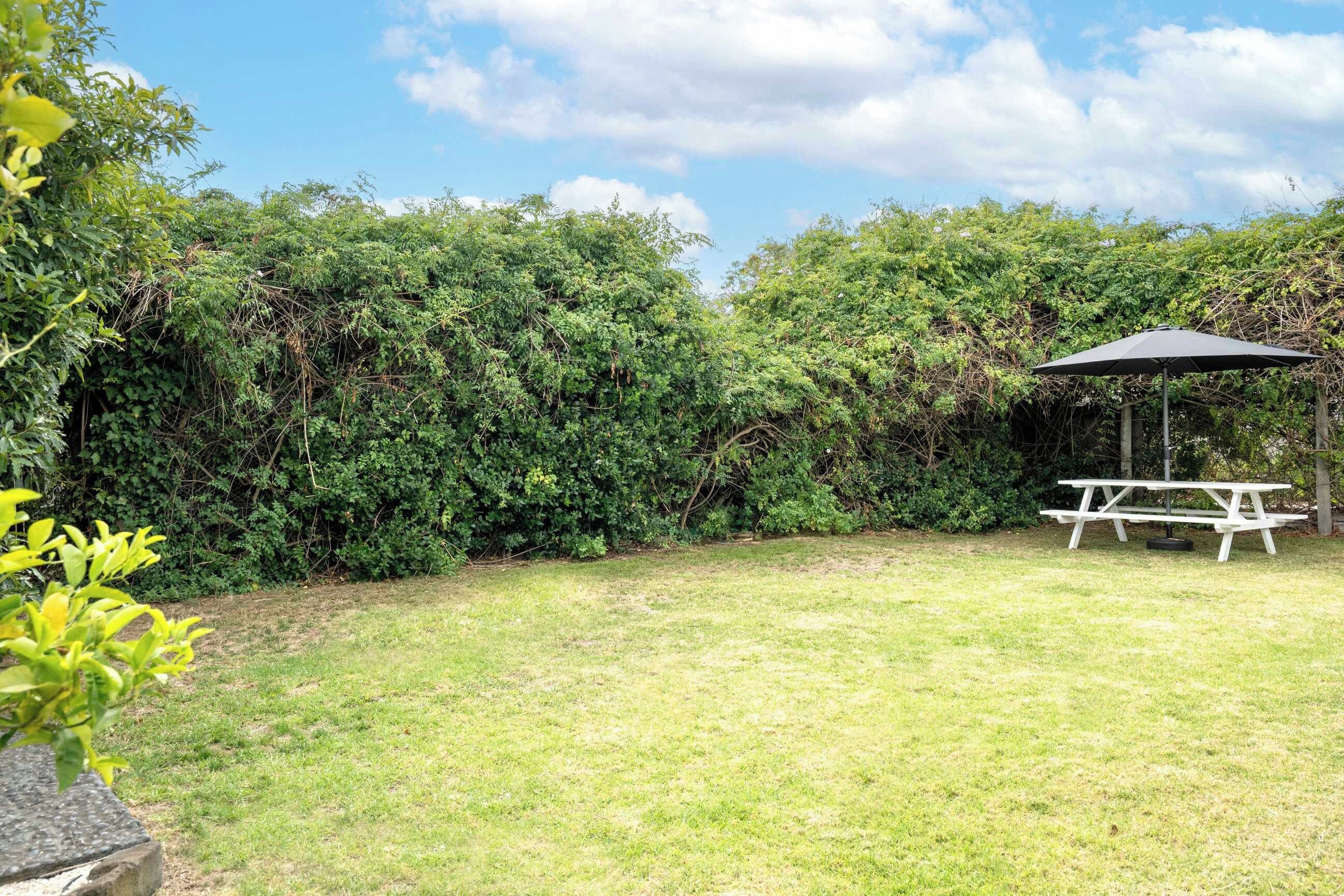 A grassy backyard with dense foliage, a picnic table, and a gazebo.