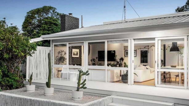 Ein modernes Haus mit großem Glasfenster, weißer Fassade und einem Kaktus im Garten.