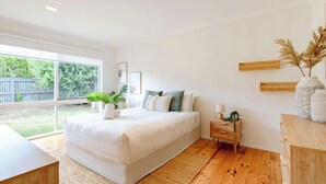 Ein Schlafzimmer mit einem großen Bett, einem Nachttisch, einem Beistelltisch und einem Fenster mit Blick ins Freie.