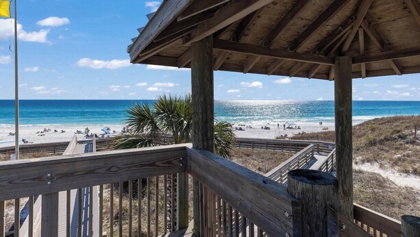 Une terrasse en bois donnant sur une plage, avec une vue dégagée sur l’océan et les personnes qui se promènent sur la plage.