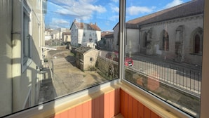Ein Zimmer mit großem Fenster mit Blick auf eine Straße, gesäumt von Gebäuden, mit einem roten Auto am Straßenrand.