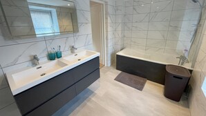 Ein modernes Badezimmer mit zwei Waschbecken, einem großen Spiegel und einer Badewanne.