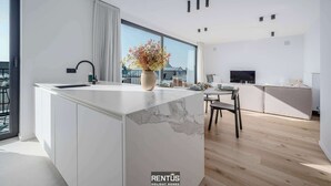 Una cocina moderna con una isla de mármol, un comedor con mesa y sillas, y un amplio ventanal con vistas a la ciudad.