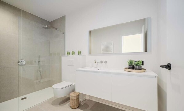 A modern bathroom with a glass-enclosed shower, a white toilet, and a vanity with a mirror and two potted plants.