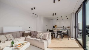 Una sala de estar moderna con un sofá, comedor y cocina. Hay un ventanal que ofrece vistas al exterior.