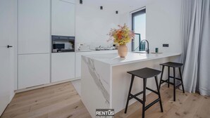 Una cocina moderna con armarios blancos, una isla de mármol, dos taburetes negros y un florero con flores.