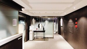 A modern hotel lobby with a reception desk, a small table with a mirror, and a glass door leading to elevators. - Feeling Motel (Gwangmyeong)