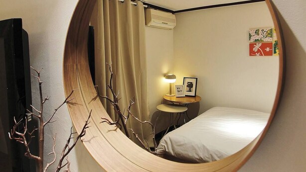 A round mirror reflecting a room with a bed, a nightstand with a lamp, a picture frame, and a wall with a small artwork. - Feeling Motel (Gwangmyeong)