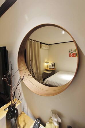 A round mirror reflecting a room with a bed, a nightstand with a lamp, a picture frame, and a wall with a small artwork. - Feeling Motel (Gwangmyeong)