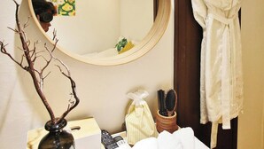 A bathroom with a round mirror, a robe hanging on a rack, a towel rack with towels, a vase with branches, a box, and a remote control. - Feeling Motel (Gwangmyeong)