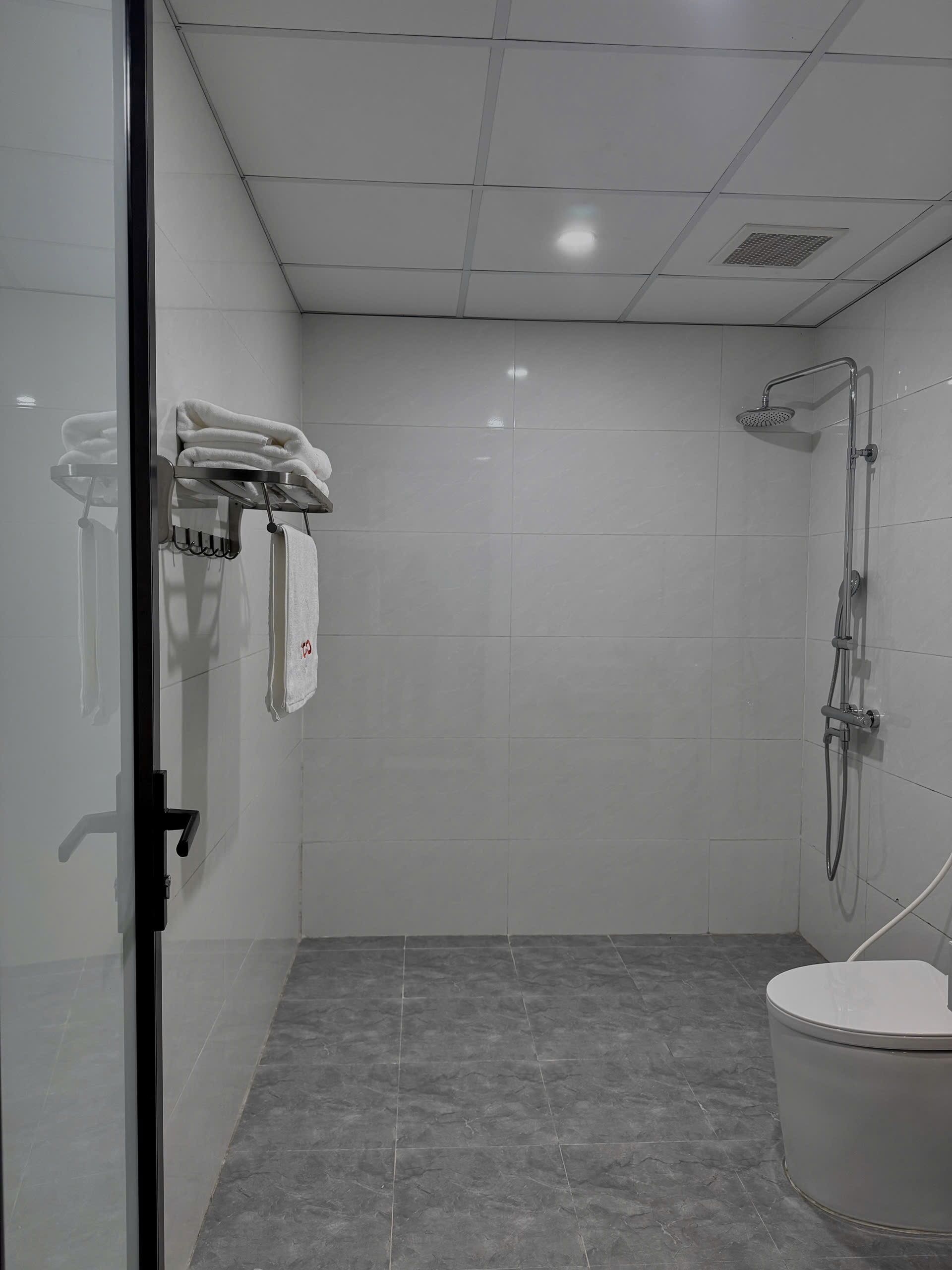 A modern bathroom with a glass shower enclosure, a toilet, and a towel rack with folded towels.