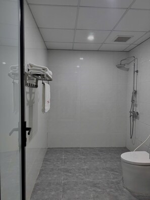 A modern bathroom with a glass shower enclosure, a toilet, and a towel rack with folded towels. - TCICO Hotel (Phan Dinh Phung)