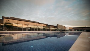 A modern building with a large glass facade, a swimming pool with a tiled deck, and a clear sky. - 55 Una -  Spa Access and Free Parking (Carbis Bay)