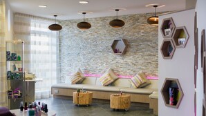 A modern spa room with a stone wall, a beige sofa with striped cushions, wooden side tables, and pendant lighting. - 55 Una -  Spa Access and Free Parking (Carbis Bay)
