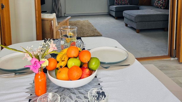 Ein Essbereich mit einem Tisch für zwei Personen, einer Obstschale und einer Blumenvase.