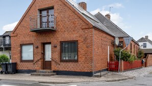 Un bâtiment en briques rouges, doté d’un toit triangulaire, d’un petit balcon et d’une porte au-dessus de laquelle est accrochée une enseigne.