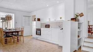 Une cuisine moderne avec des meubles blancs, un coin repas doté de chaises en bois et un escalier menant à l’étage supérieur.
