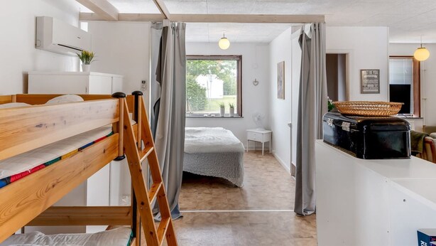 Une chambre moderne et bien éclairée, avec un lit superposé, une échelle, un bureau avec un panier et une fenêtre avec des rideaux.