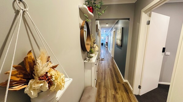 Un pasillo con un tapiz de macramé en la pared, piso de madera y una puerta a la derecha.