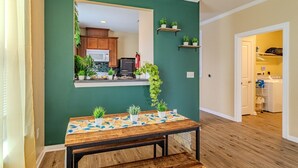 Un coin repas avec une table, des chaises et un banc. On aperçoit une cuisine à travers un miroir, et une buanderie au fond.