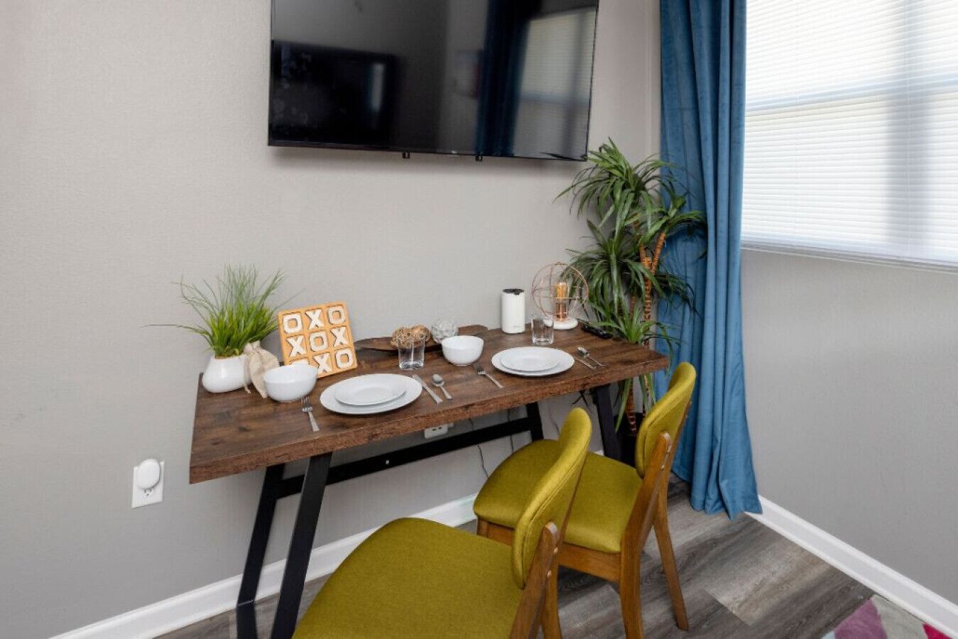 Un coin repas avec une table en bois, deux chaises, un téléviseur fixé au mur et une plante en pot.