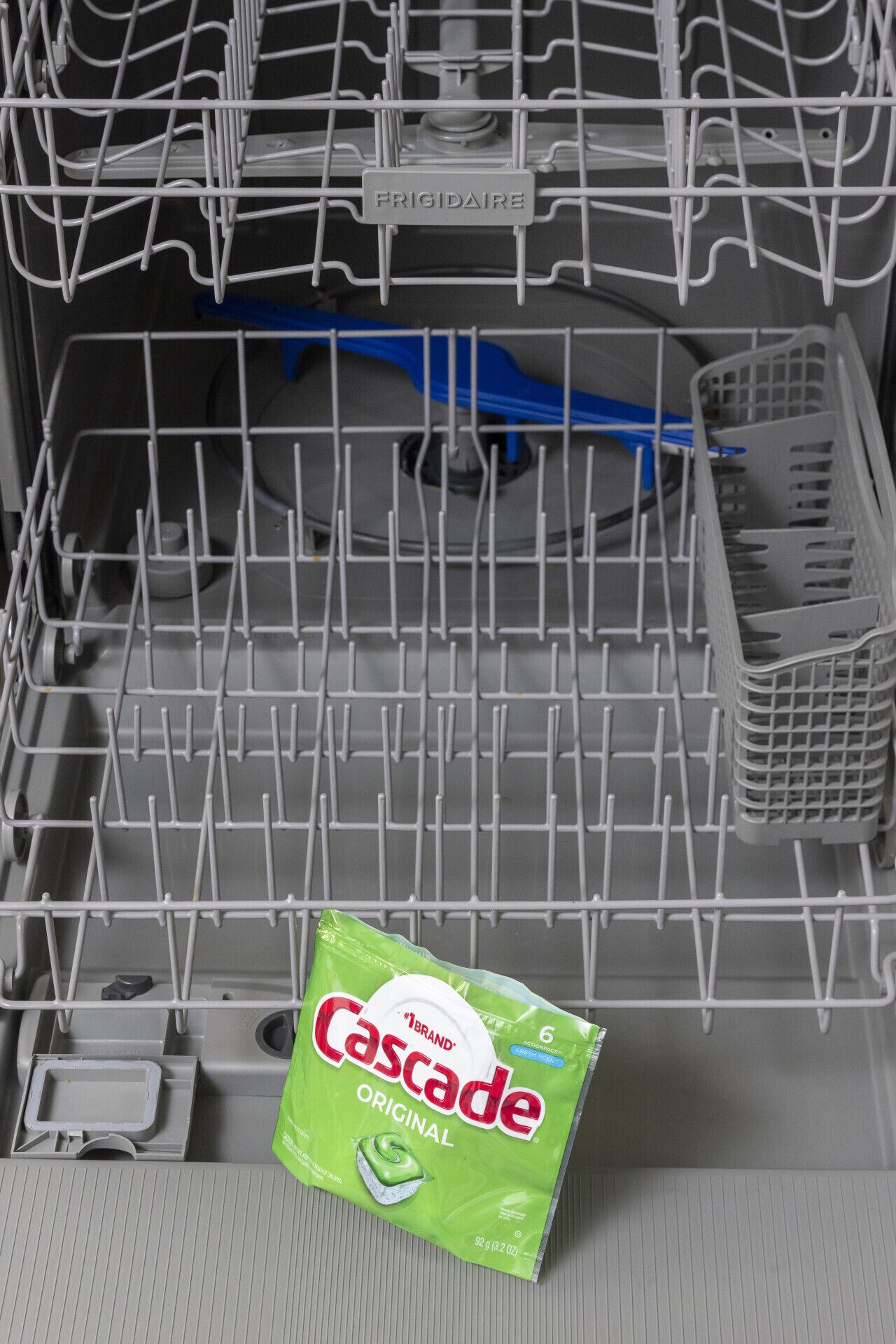 A dishwasher with a green Cascade Original detergent packet on the bottom rack.
