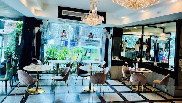 A modern interior with round tables and chairs, a large chandelier, and a view through a glass wall. - The Class Boutique Hotel (Pattaya)