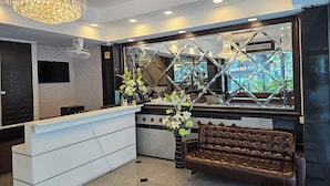 A reception area with a white counter, a brown leather sofa, a large mirror reflecting the interior, and a chandelier. - The Class Boutique Hotel (Pattaya)