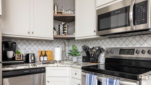 A kitchen with white cabinets, a stainless steel microwave, a black stove, and a coffee maker. - Modern City Oasis: Pet Friendly | Downtown | Park (Little Rock)