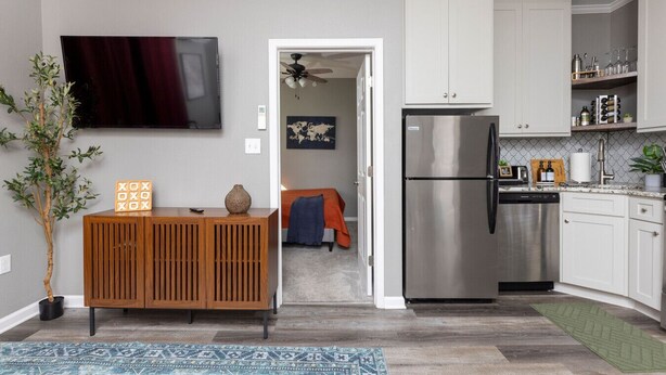 A modern kitchen with a stainless steel refrigerator, white cabinets, and a wooden cabinet with decorative items. - Modern City Oasis: Pet Friendly | Downtown | Park (Little Rock)