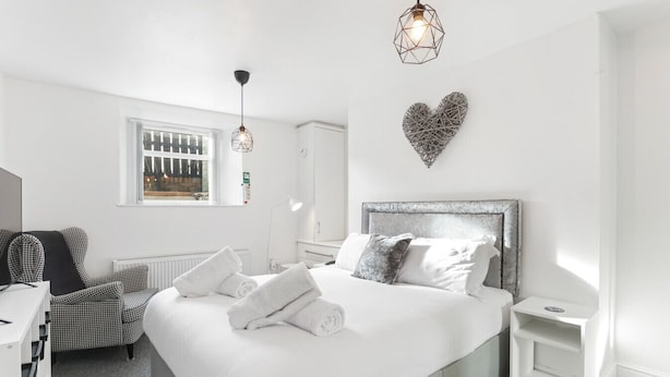Un dormitorio moderno con una cama grande, un aparador, un escritorio, una silla y una ventana con persianas.