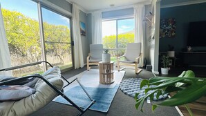 A spacious room with large windows, a ceiling fan, two chairs, a small table, and a potted plant.