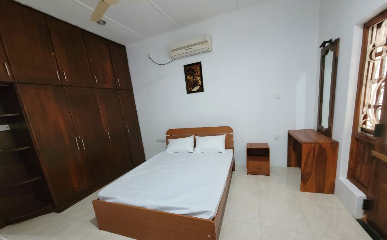 A bedroom with a wooden bed, a wardrobe, a small bedside table, and a mirror.