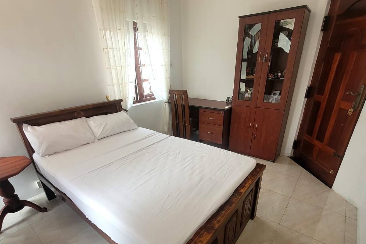 A bedroom with a wooden bed, a desk, a wardrobe, and a chair.