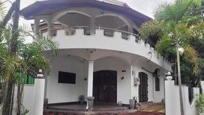 A white building with a covered porch, a large wooden door, and a red and black striped carpet. - Grace- The Joyful Rest (Batticaloa)